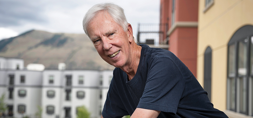 Darrell Baggs stands smiling on a balcony with multi-story apartment buildings in the background