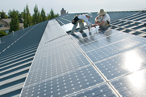 Two figures install solar panels on the top of a Whitman campus building.