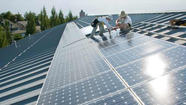 Two figures install solar panels on the top of a Whitman campus building.