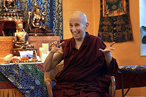Venerable Thubten Chodron sits in a chair and speaks animatedly to someone off camera.
