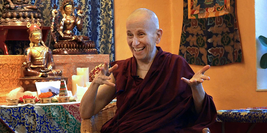 Venerable Thubten Chodron sit in a chair and speaks animatedly to someone off camera.