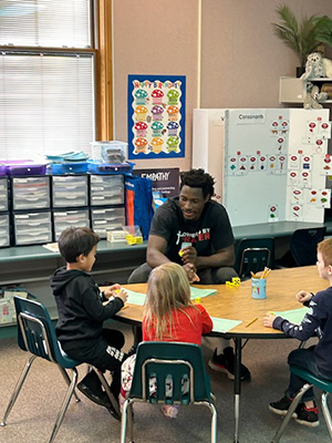 Whitman College Basketball player sitting in a classroom with elementary students