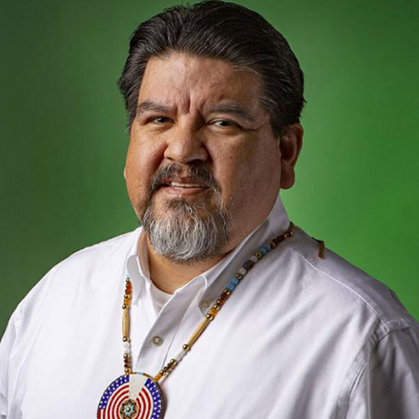 Portrait of Chuck Sams wearing a white shirt and a beaded necklace.