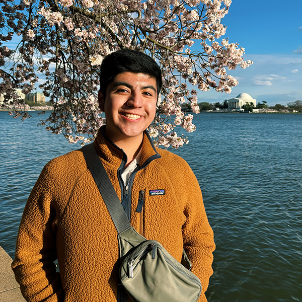 Portrait of Jose Silva, standing by a body of water with cherry blossoms behind him.