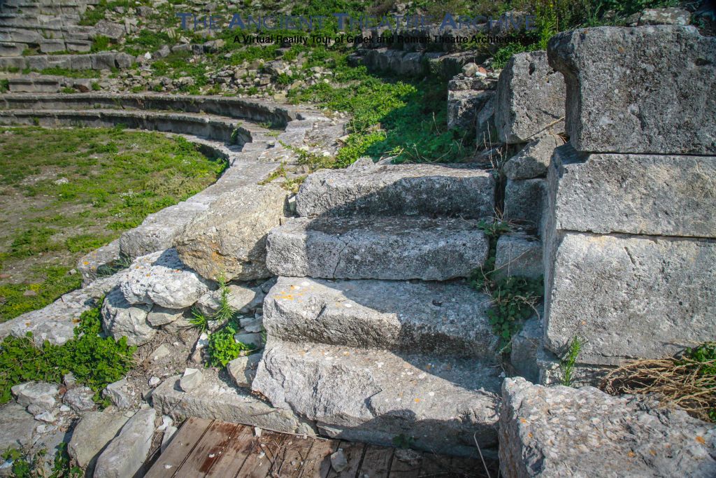 4 steps leading up from parodos to three rows of front seating (prohedriai), third row had continuous raised backs; both second and third rows have griffins’s foot terminations; reclining lion on low wall flanking ends of prohedriai; no drain around orchestra. Photo: T Hines 2019.